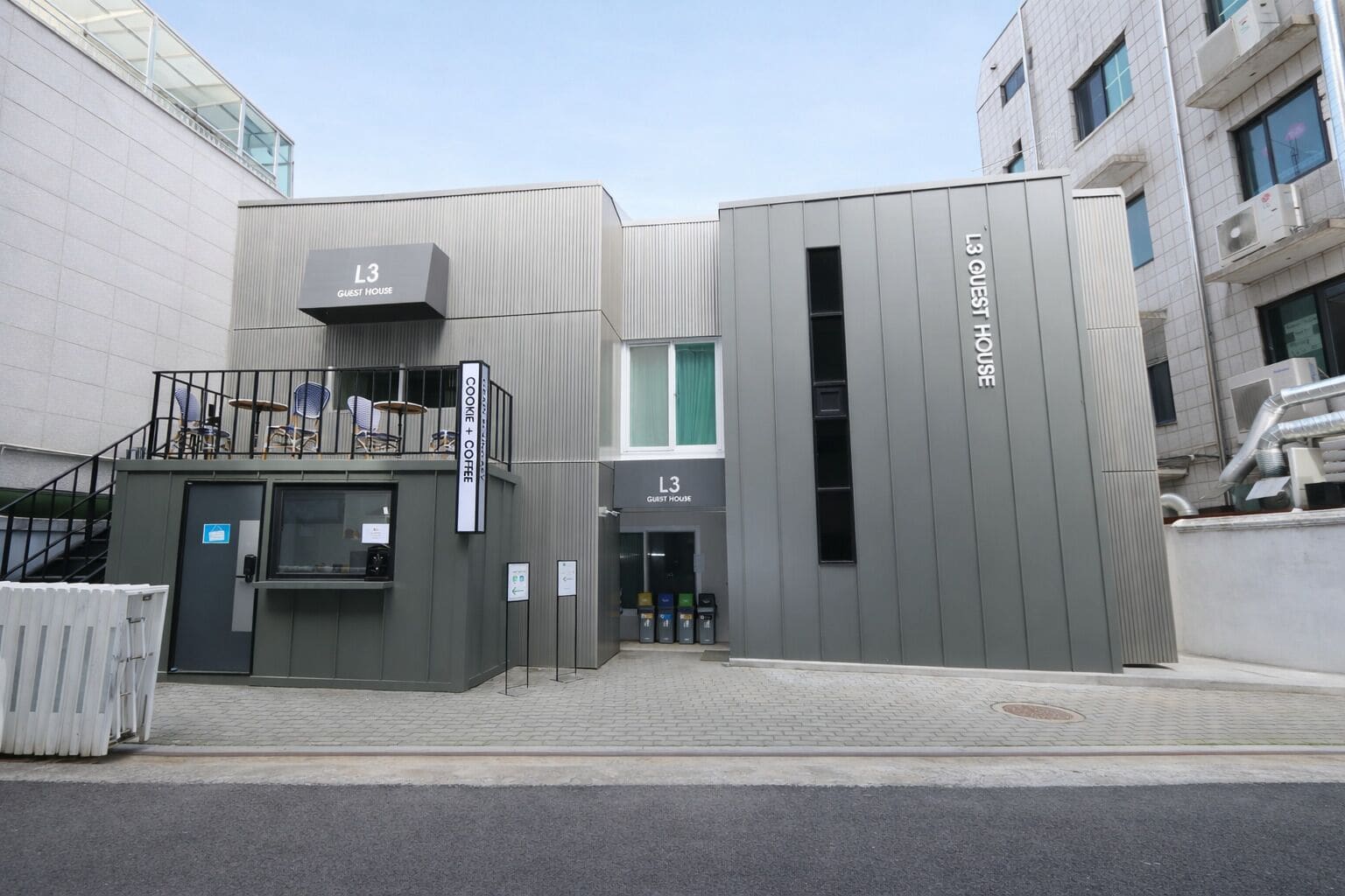 A modern building with a sign reading 'L3 GUEST HOUSE' and a smaller sign for 'COOKIE + COFFEE'.