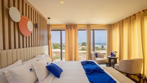 A hotel room with a large bed, a view of the beach, and a seating area with a table and chairs. - MARLIN RESORT (Nyanyanu)