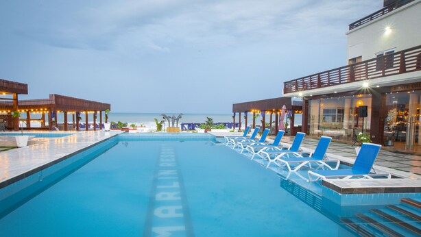 A swimming pool with lounge chairs and a view of the ocean. - MARLIN RESORT (Nyanyanu)