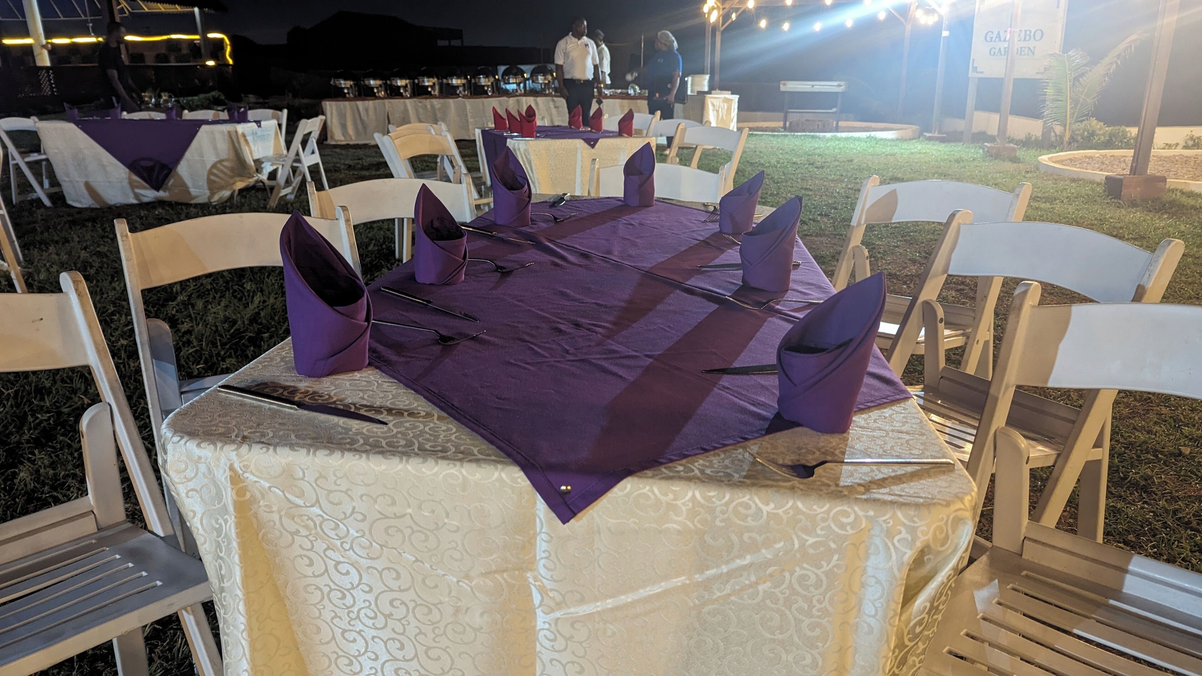 A table set outdoors with white chairs and purple napkins.