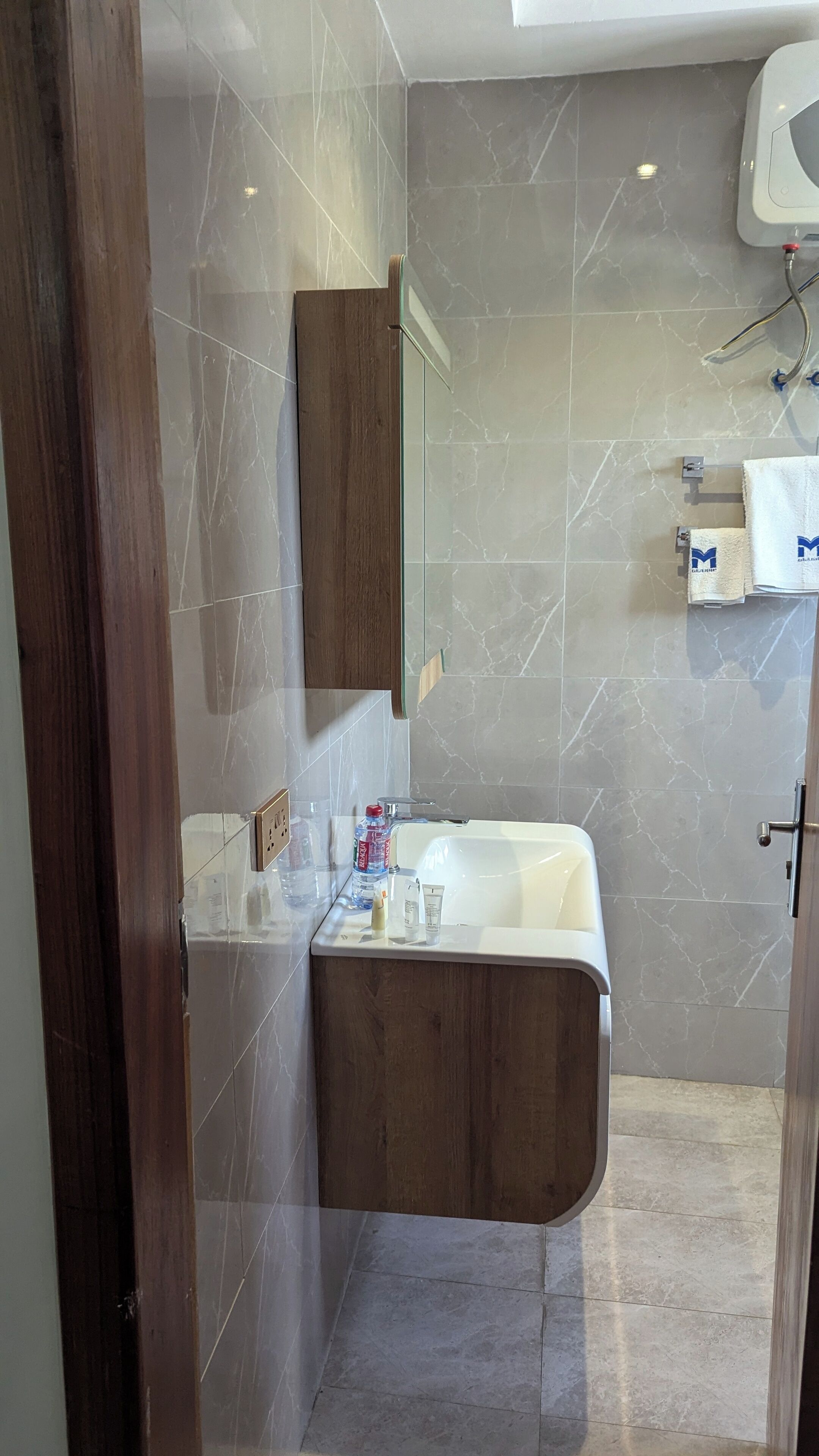 A modern bathroom with a marble floor, a wooden vanity, a white sink, and a large mirror.