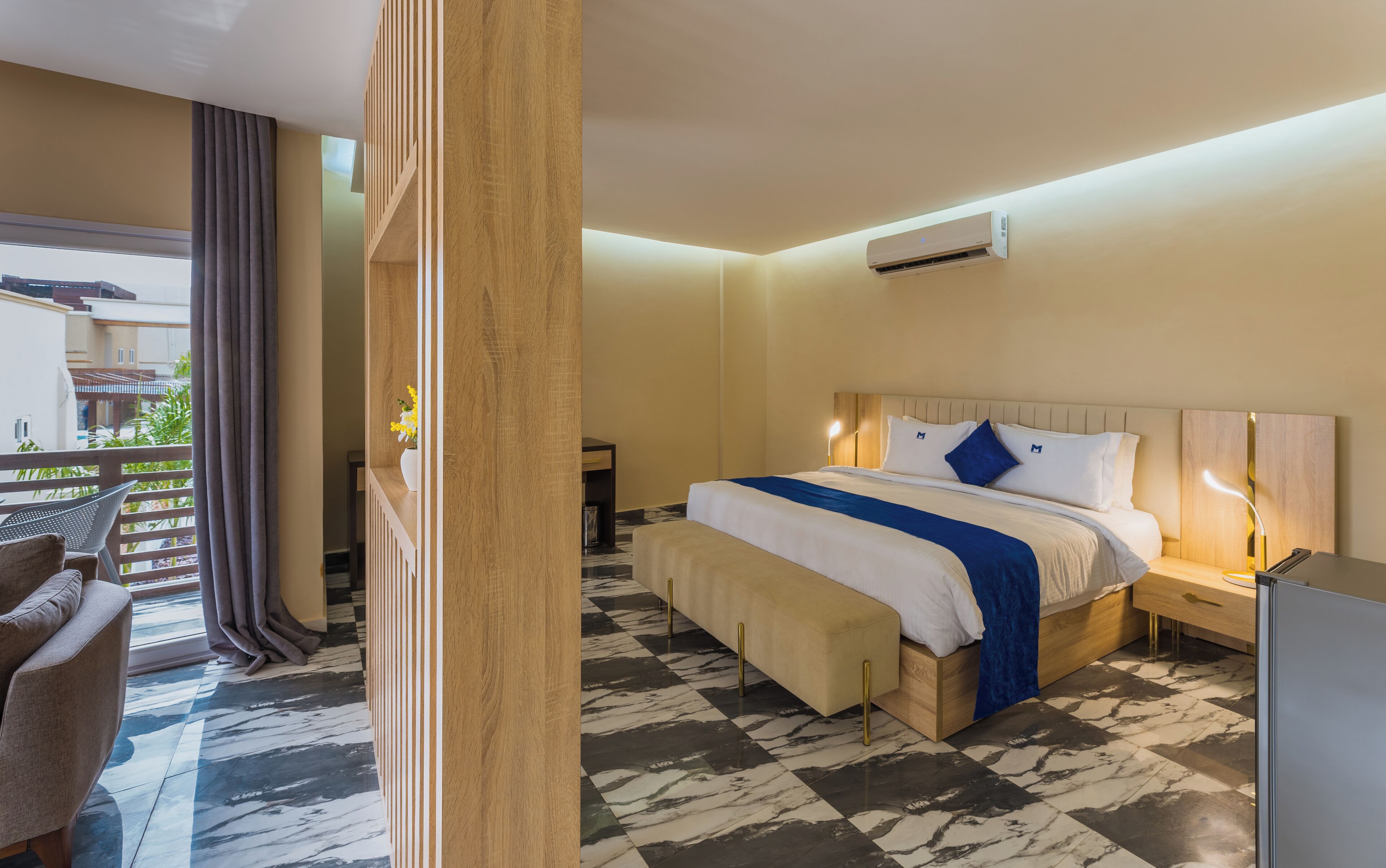 Habitación de hotel con cama, mesita de noche y vista al balcón exterior.