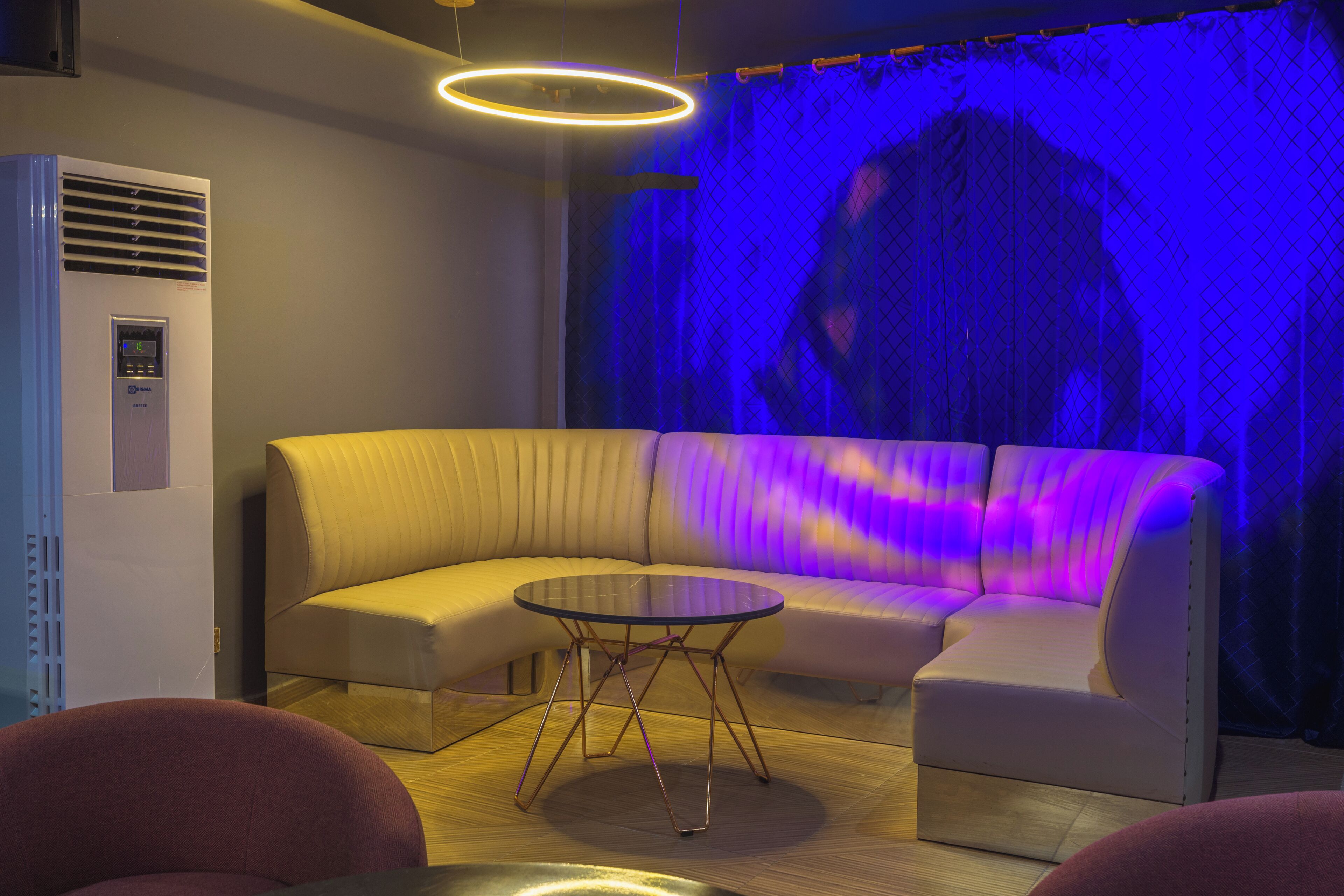 A modern lounge area with a curved sofa, a glass coffee table, and a wall-mounted air conditioning unit.