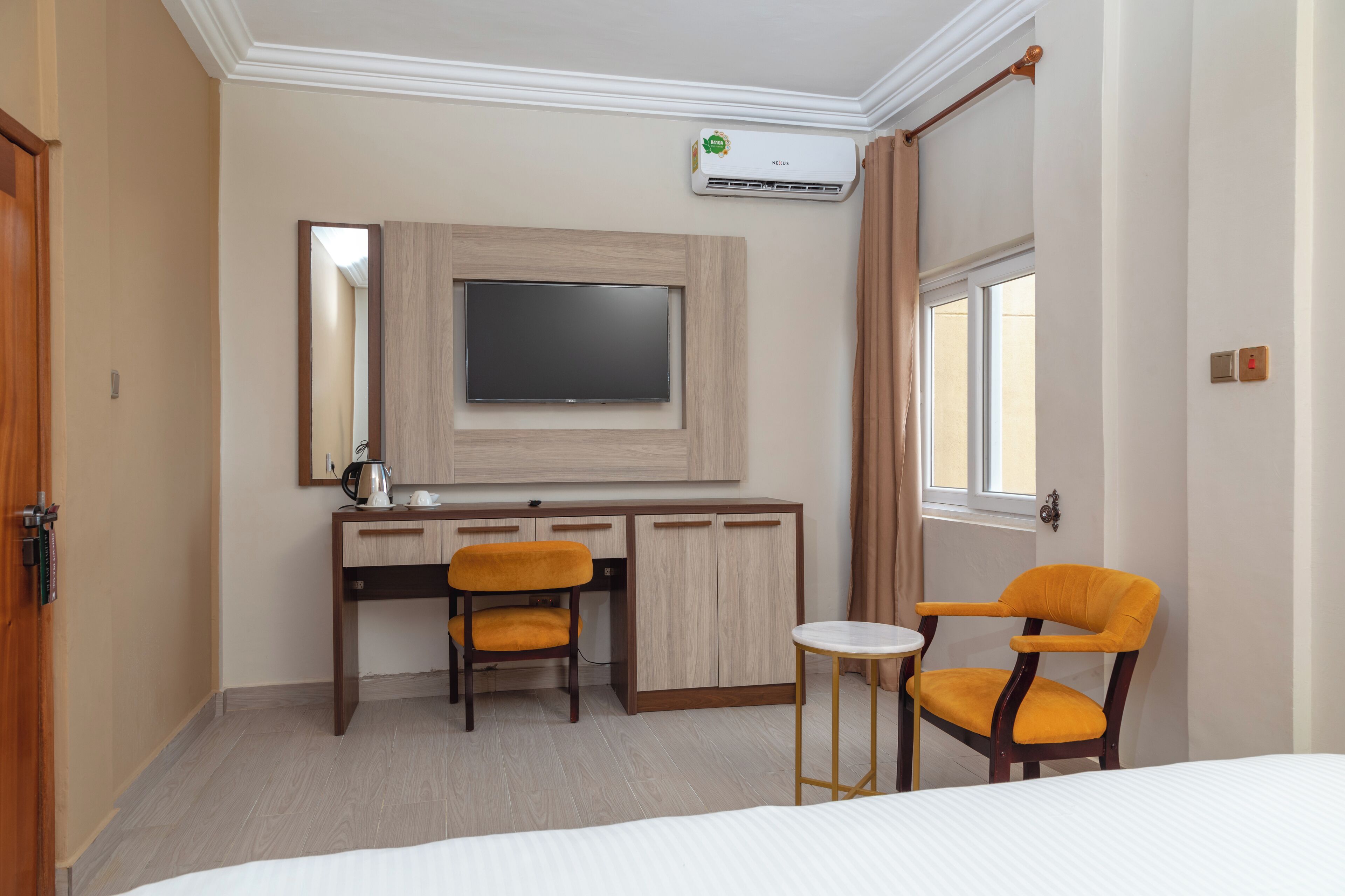 A hotel room with a bed, a desk with two chairs, a television, and an air conditioning unit.