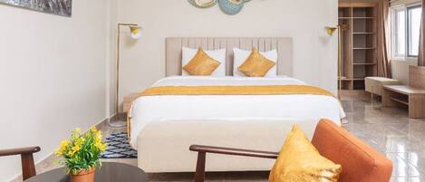 A hotel room with a bed, a seating area with a table and chairs, a potted plant, and a decorative wall piece.