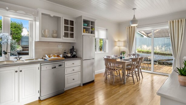 A modern kitchen with white cabinetry, a wooden dining table, and a view of the garden through large sliding glass doors. - An tSean Scoil, Clifden in the heart of clifden town (Clifden)