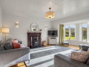 A living room with a fireplace, sofa, television, and large windows.