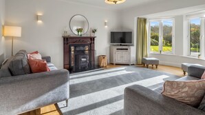 A modern living room with a fireplace, a television, and a large window with a view of greenery. - An tSean Scoil, Clifden in the heart of clifden town (Clifden)