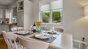 A dining area with a table set for four, white chairs, a vase with flowers, and a bottle of wine. - An tSean Scoil, Clifden in the heart of clifden town (Clifden)