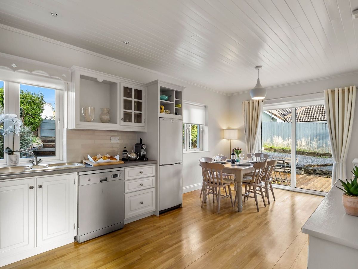 A modern kitchen with white cabinetry, a built-in dishwasher, and a dining area with a table and chairs.