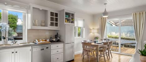 A modern kitchen with white cabinetry, a built-in dishwasher, and a dining area with a table and chairs.
