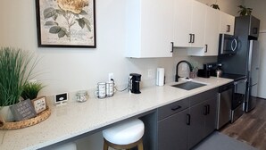 Une cuisine moderne avec des meubles blancs, des appareils en acier inoxydable et un coin café.