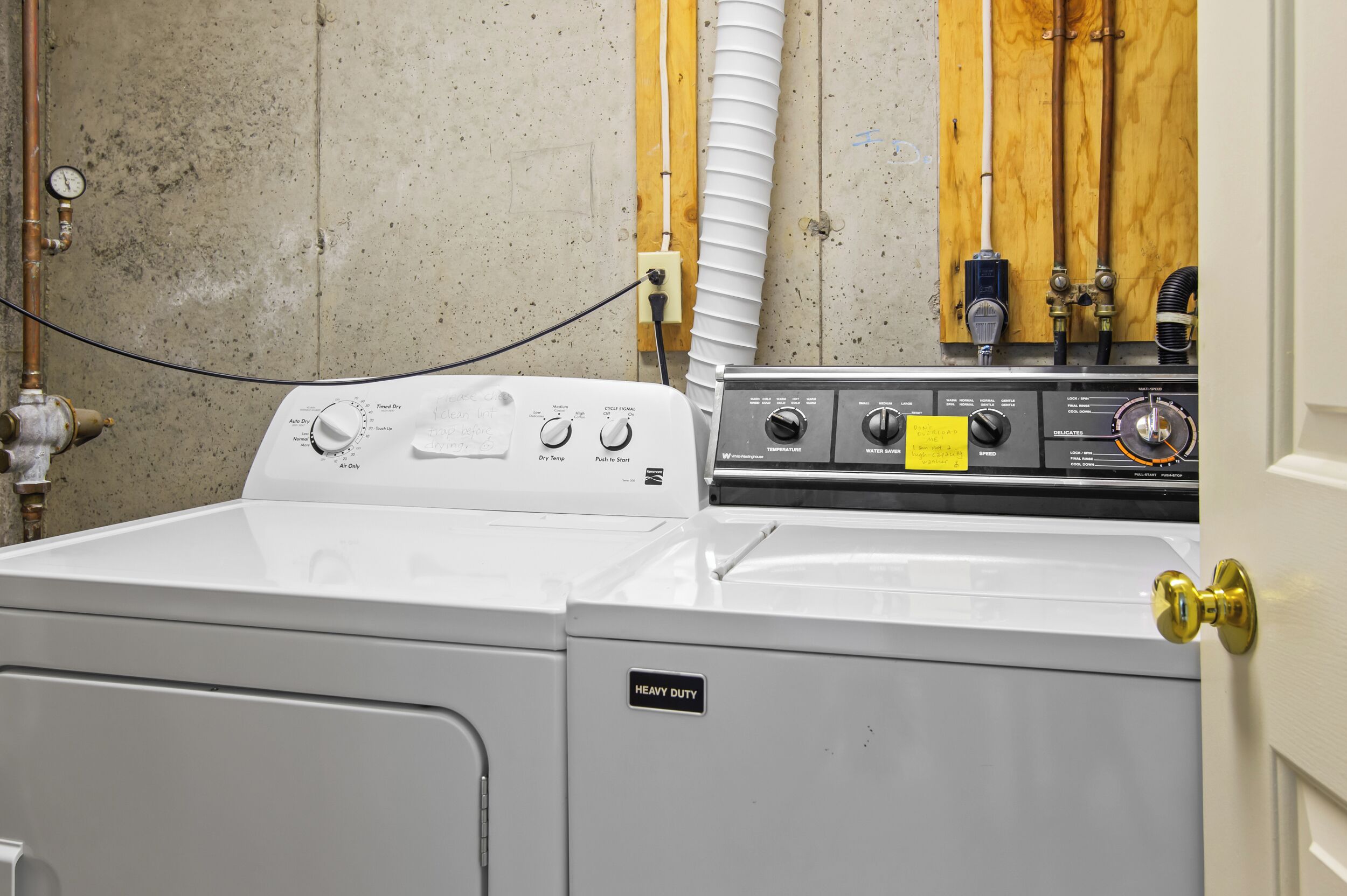 A front-loading washer and dryer unit with a control panel, a pressure gauge, and a water inlet valve.