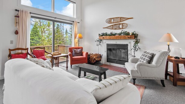 A spacious living room with a fireplace, large windows, and a balcony. - Saddleback - Rock Pond Condo 43 - ski in/out, pet friendly! (Rangeley)