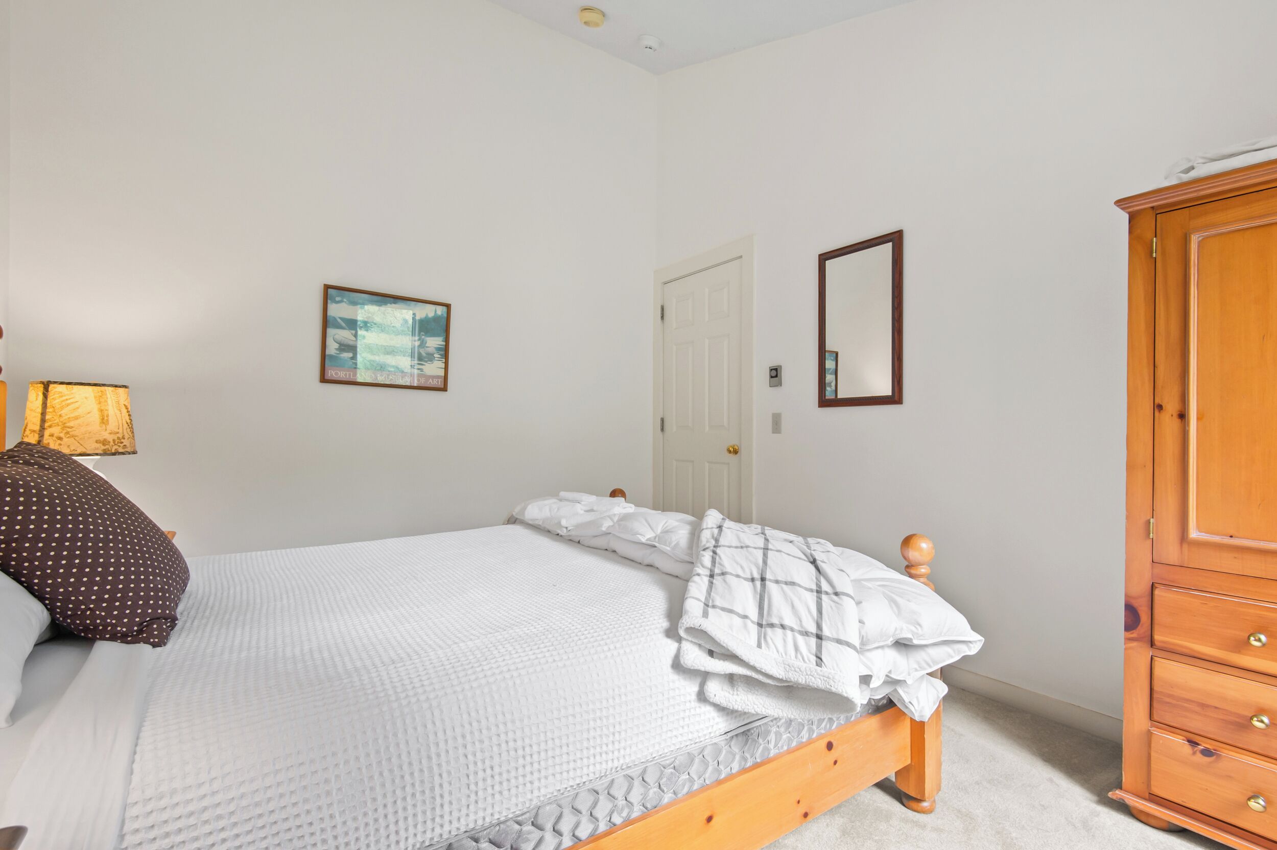 Une chambre à coucher avec un lit, une armoire en bois, une porte et un tableau encadré au mur.
