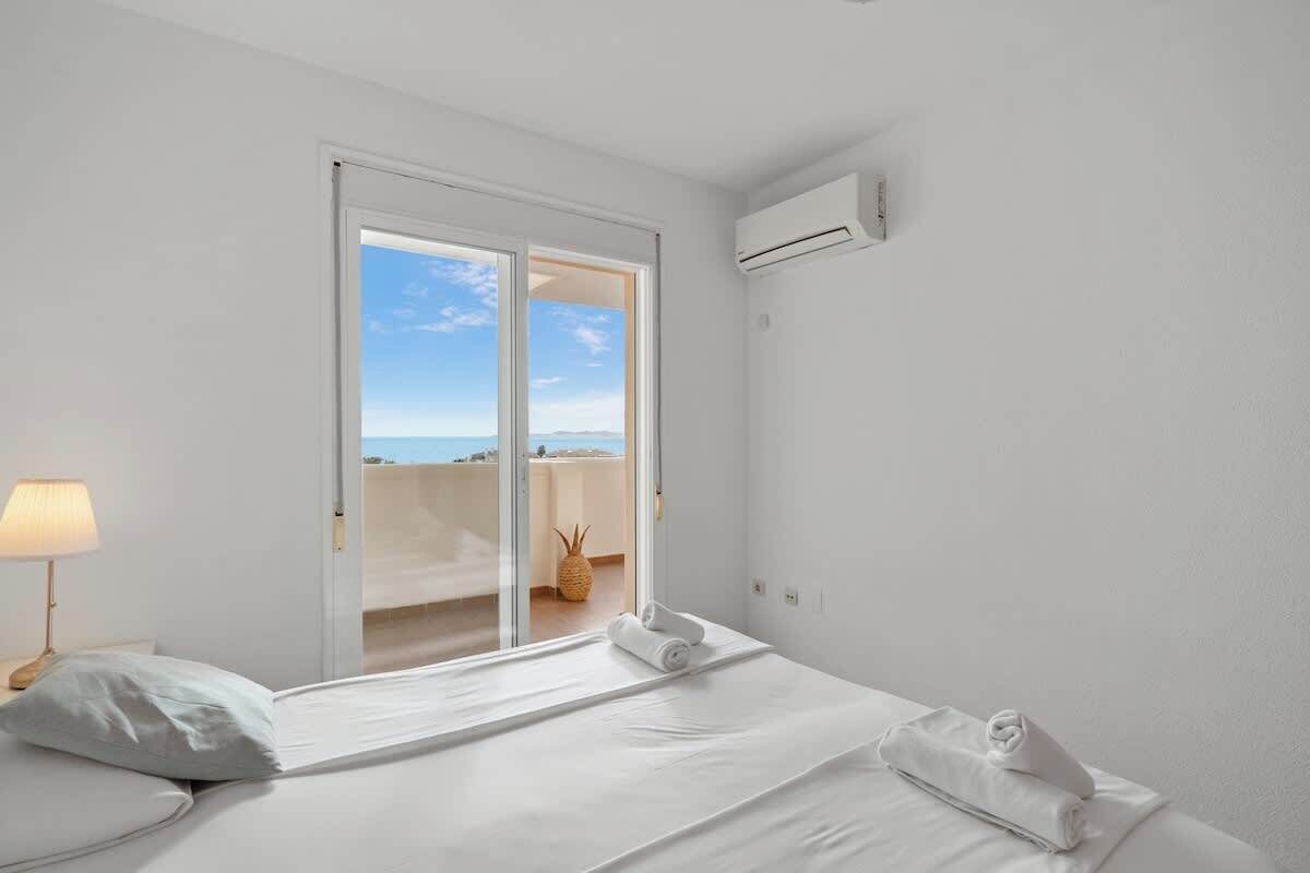 Une chambre d’hôtel avec un lit, une lampe, une fenêtre donnant sur un paysage agréable et un appareil de climatisation.