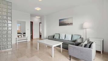 Un salon moderne avec un canapé gris, une table basse blanche et un fauteuil gris. Un tableau est accroché au mur et une lampe sur pied se trouve sur une table d’appoint.
