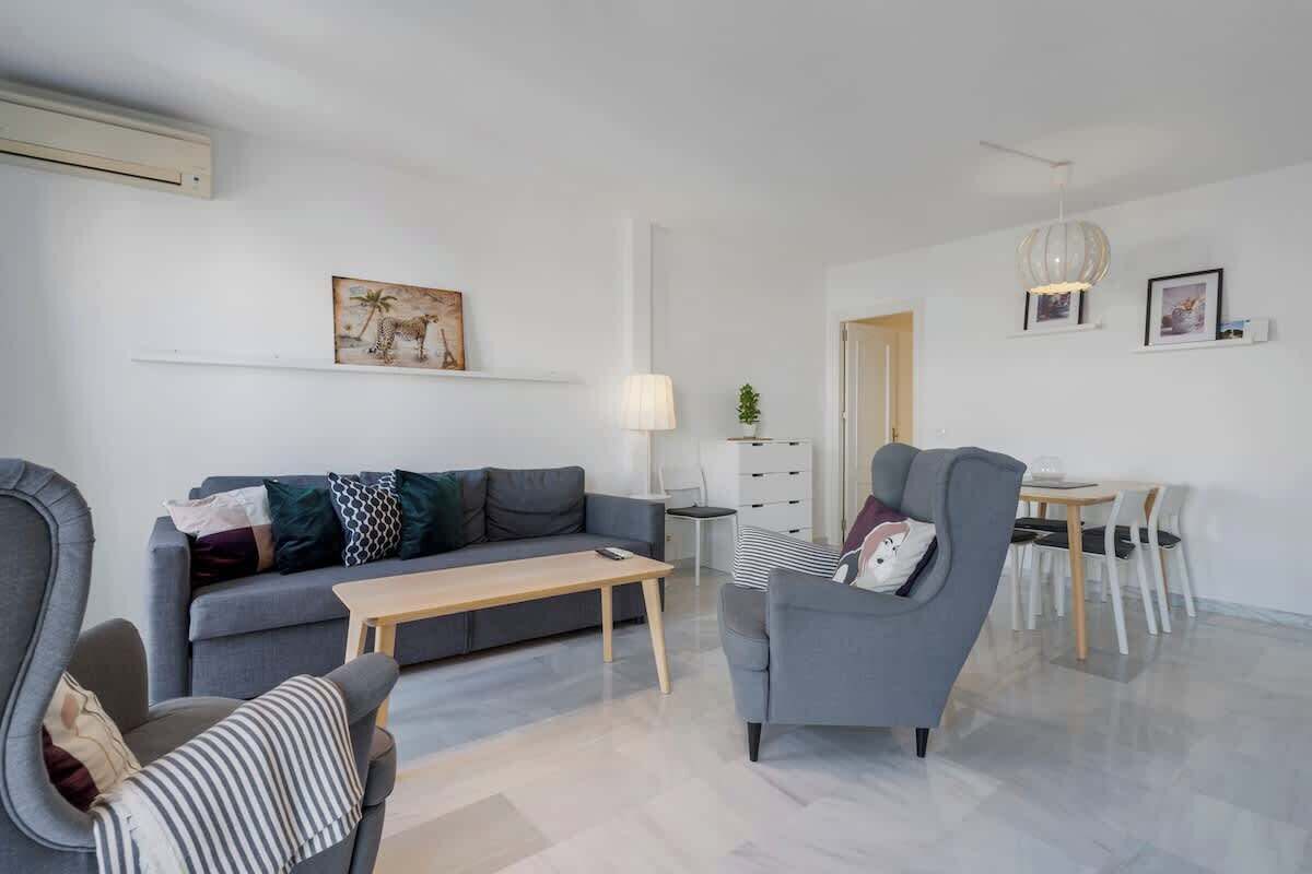 Een moderne woonkamer met een grijze bank, een gestreept fauteuil, en een eethoek met een tafel en stoelen.