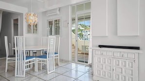 A room with a white dining table, chairs, and a white cabinet. There is a window with a view of buildings outside. - Benalmadena over the sea by Costarentals - Ref 17 (Benalmádena)