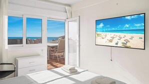 A hotel room with a bed, a desk, and a chair. There is a large window with a view of the beach and ocean. - Benalmadena over the sea by Costarentals - Ref 17 (Benalmádena)