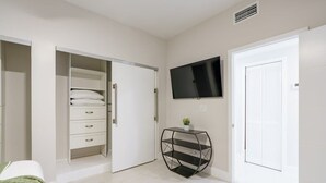 Ein Schlafzimmer mit einem Bett, einem Kleiderschrank, einem Fernseher und einem kleinen Tisch mit einer Pflanze.