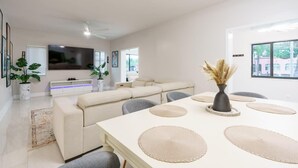 Ein modernes Wohnzimmer mit einem weißen Sofa, einem Esstisch mit Platzsets und einem an der Wand montierten Fernseher.