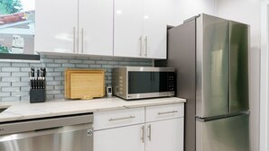 Eine moderne Küche mit weißen Schränken, einem Edelstahlkühlschrank, einer Mikrowelle und einem Geschirrspüler.