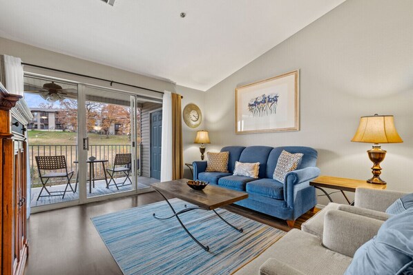 A living room with a blue sofa, a coffee table, and a view of a courtyard through a sliding glass door. - Enjoy the peaceful views, or take a short drive to all the fun! (Branson)