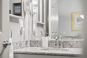 A bathroom with a granite countertop, a white sink, a mirror, a hairdryer, and a framed picture on the wall. - Enjoy the peaceful views, or take a short drive to all the fun! (Branson)