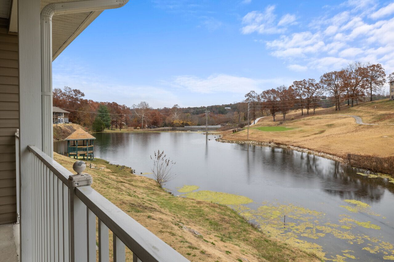 A lakeside view from a porch with a gazebo, a house, and trees in the background.