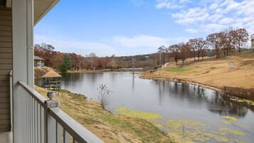A lakeside view from a porch with a gazebo, a house, and trees in the background.