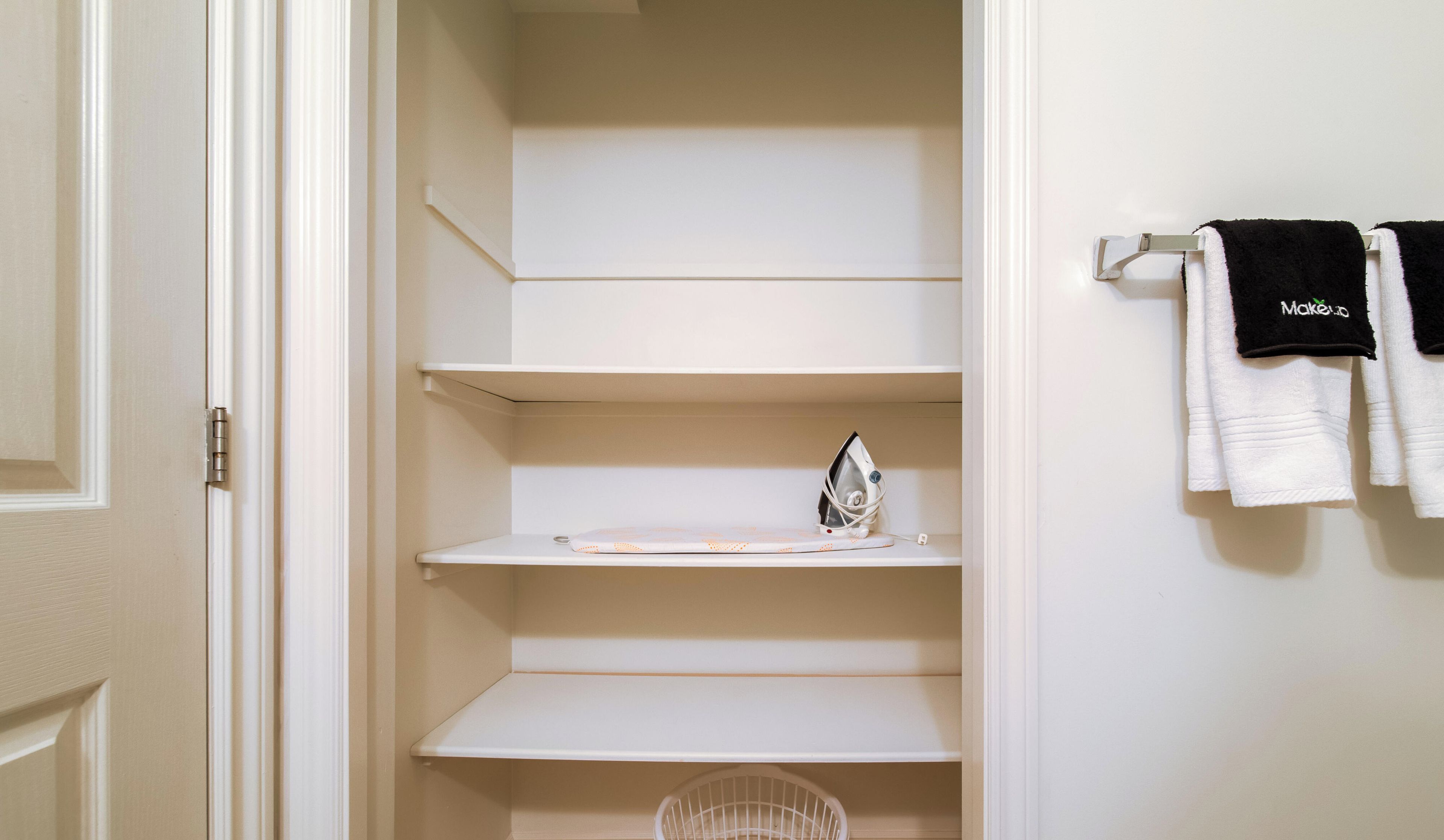 A closet with white shelves, an iron, and hanging towels.