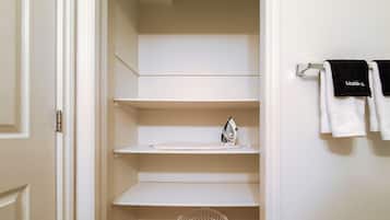 A closet with white shelves, an iron, and hanging towels.