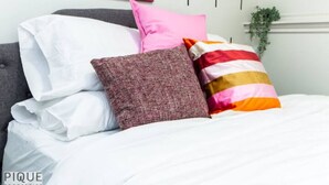 Una cama con ropa de cama blanca y varios almohadones de distintos colores y diseños.