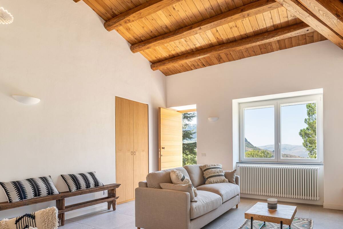 Un salon moderne avec un plafond en bois, un canapé, une table basse et une grande fenêtre donnant sur l’extérieur.