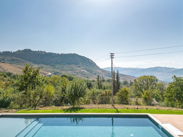 A swimming pool with a view of a hilly landscape and a power line in the background.