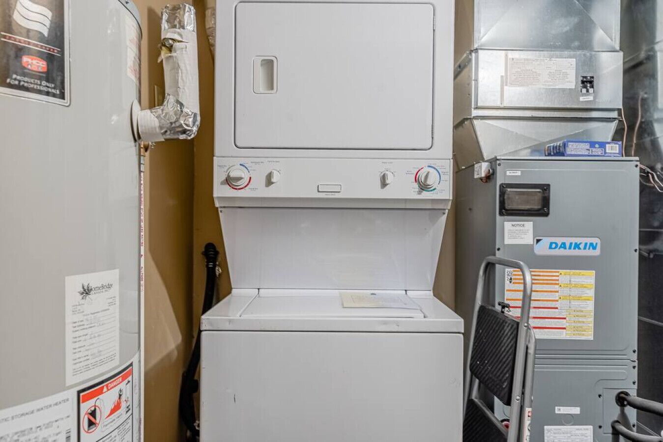 A compact, industrial-style laundry room with a front-loading washing machine, a dryer, and a Daikin air conditioning unit.
