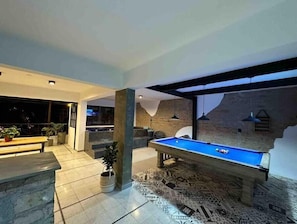 Uma área interna moderna com piscina, mesa de bilhar, plantas em vasos e uma parede de pedra.