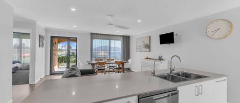 Una cocina moderna con lavavajillas integrado, comedor con mesa y sillas, y un amplio ventanal con vistas al exterior.