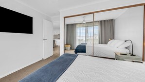 Ein Hotelzimmer mit einem großen Bett, einem an der Wand montierten Fernseher, einem Nachttisch mit Lampe und Blick auf die Stadt durch das Fenster.