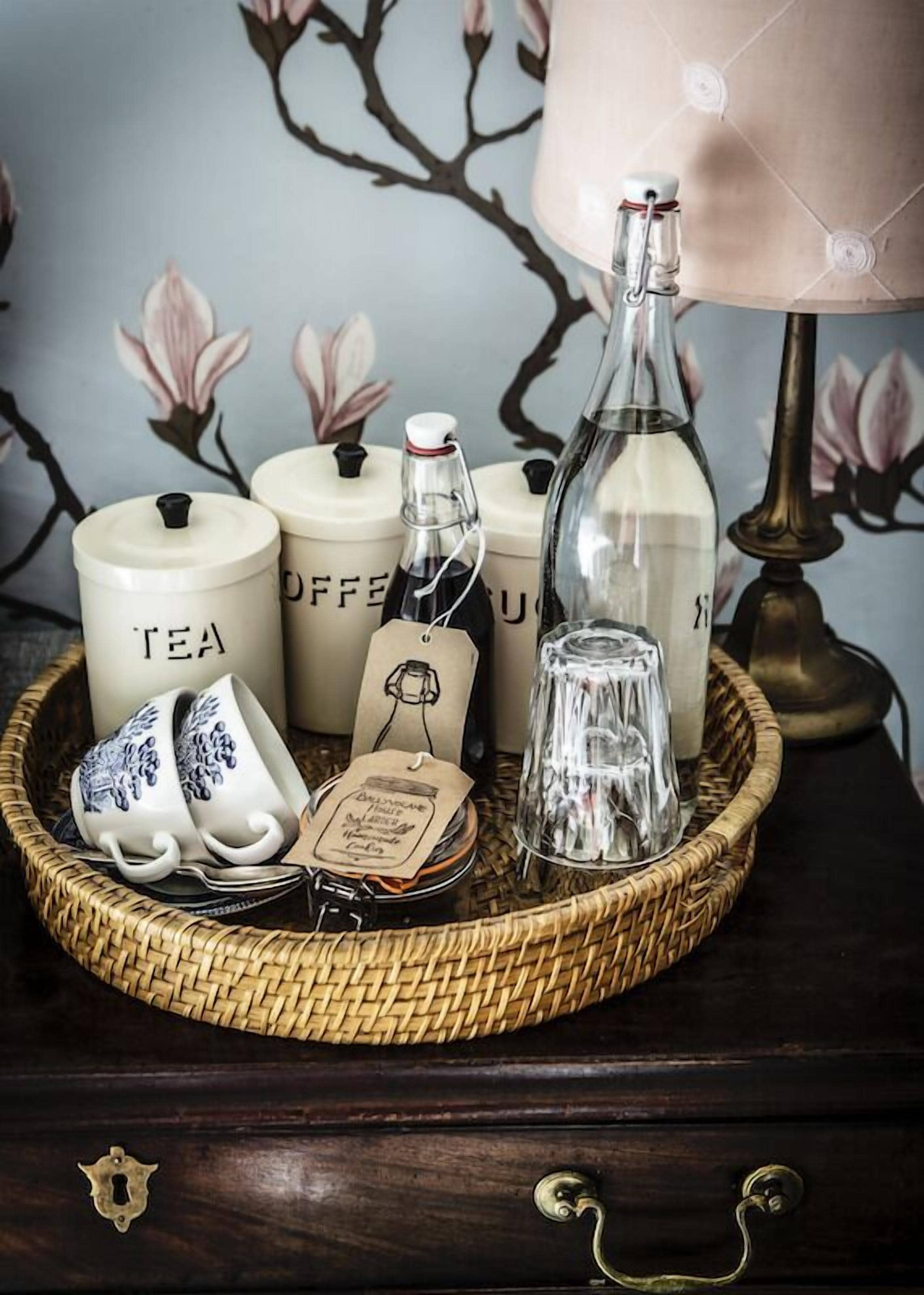 A tray with tea and coffee containers, a glass bottle, and ceramic cups on a dark wooden surface.