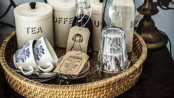 A tray with tea and coffee containers, a glass bottle, and ceramic cups on a dark wooden surface.