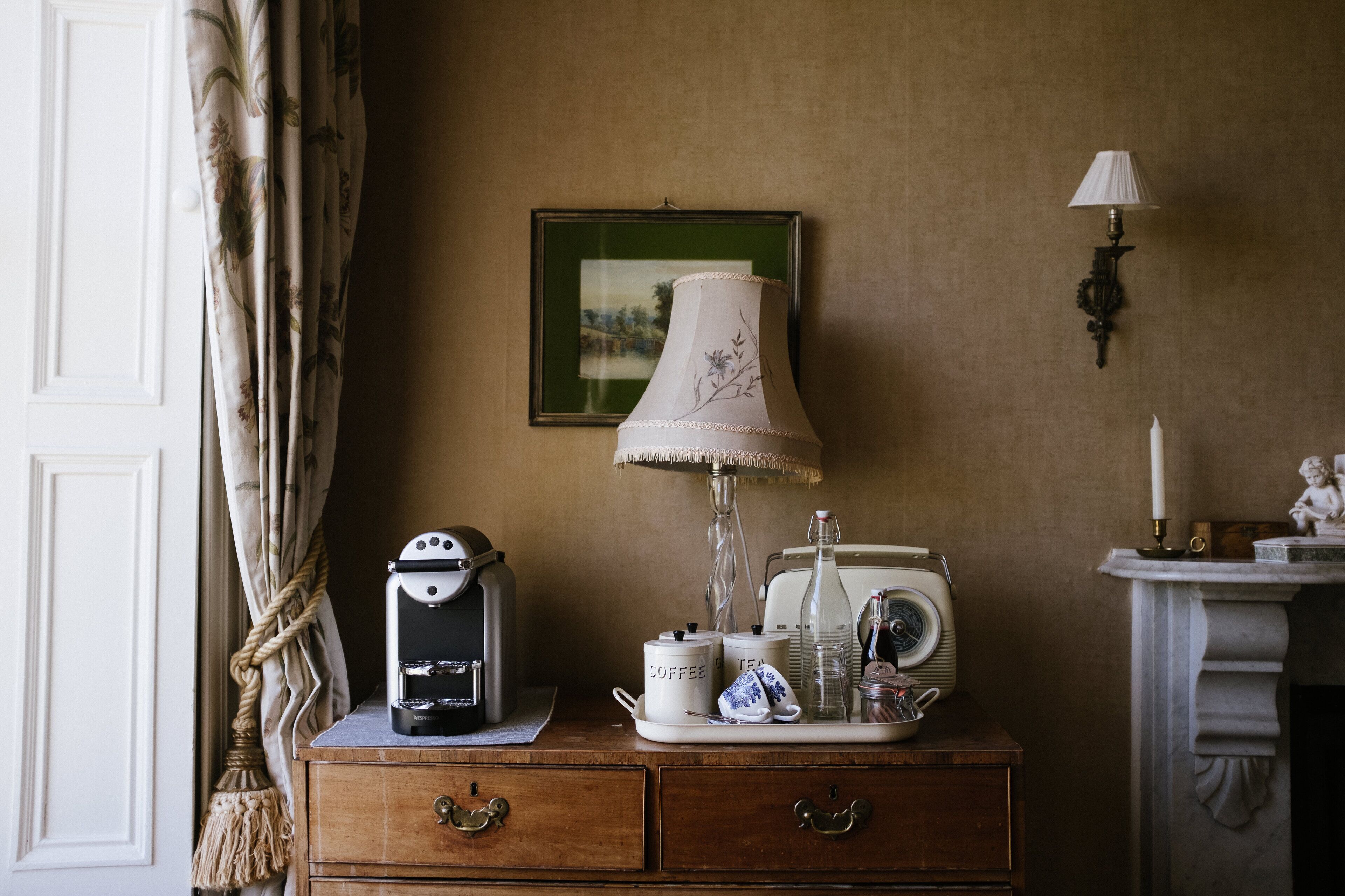 Habitación de estilo antiguo con cómoda de madera, radio vintage, cafetera y lámpara.