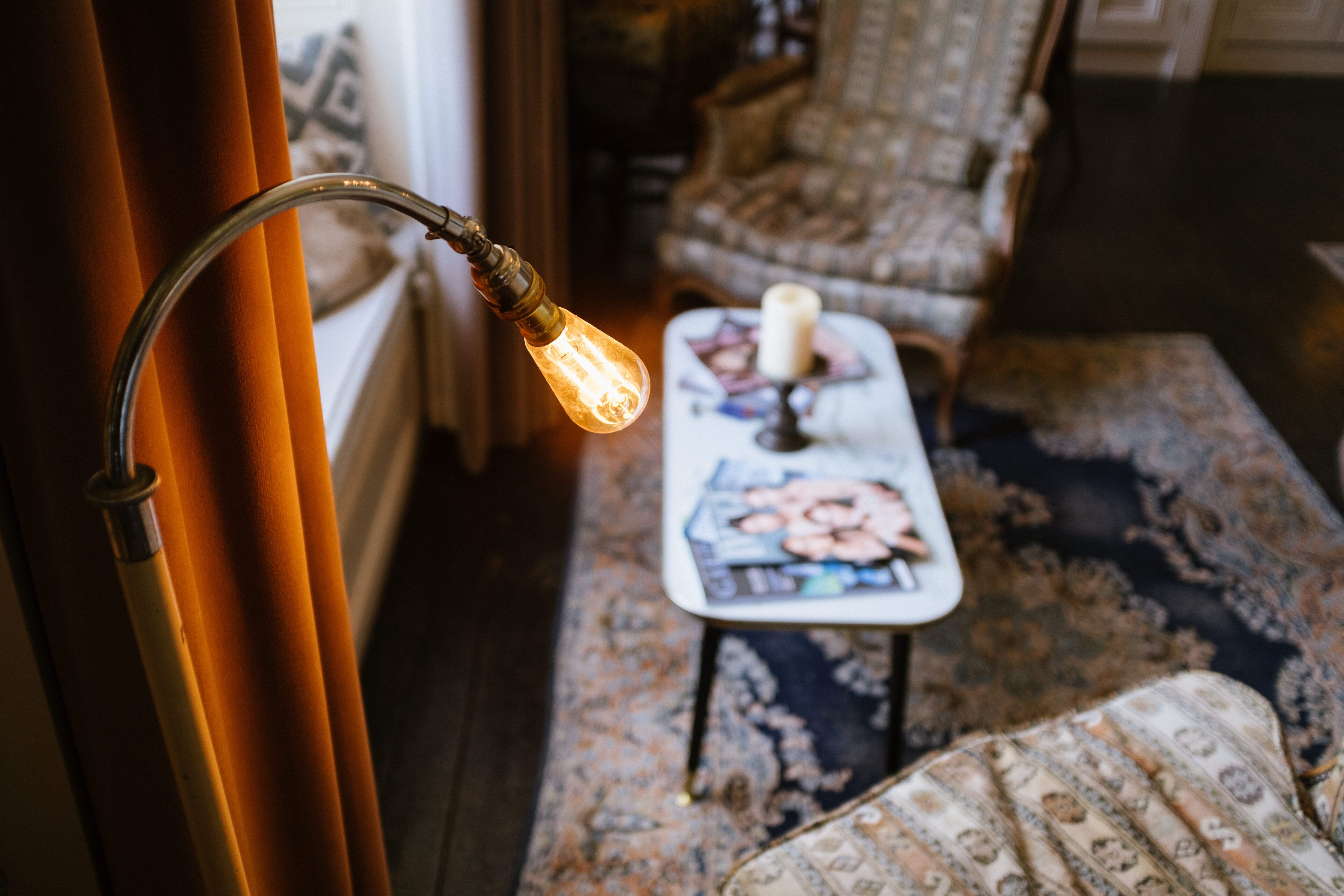 Een kamer met een lamp in vintage-stijl, een kamerbreed tapijt met patroon en een klein tafeltje met een kaars.