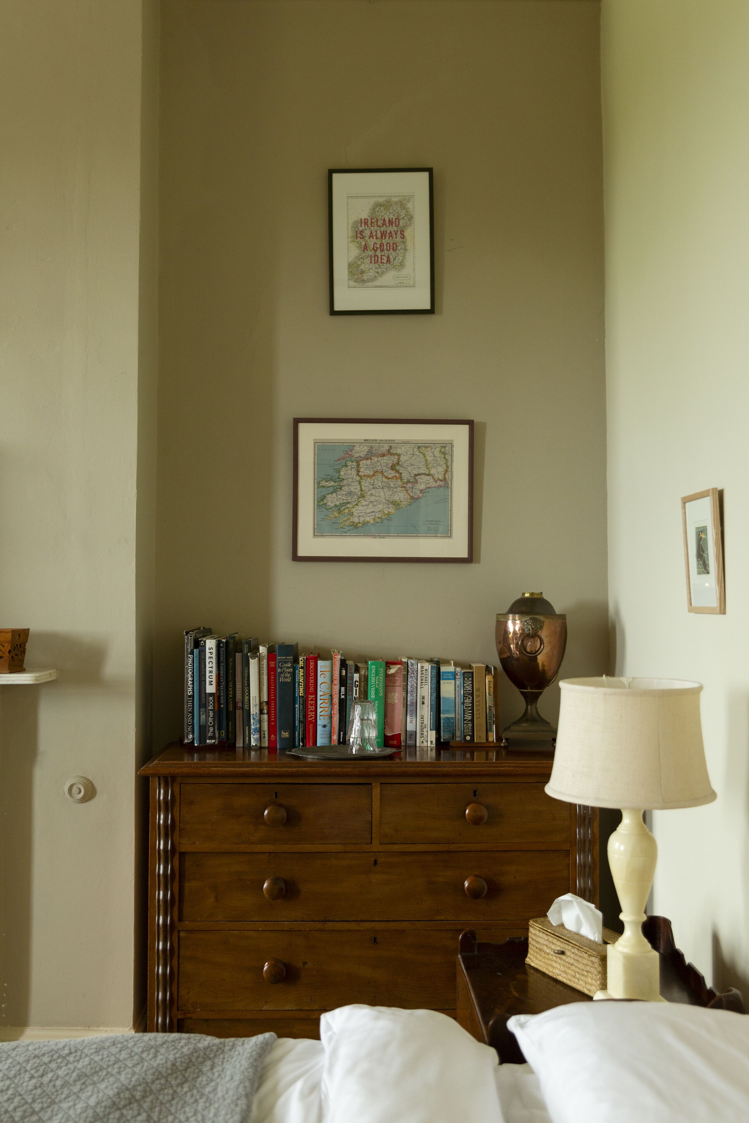 A bedroom with a wooden dresser, a map, and a lamp.