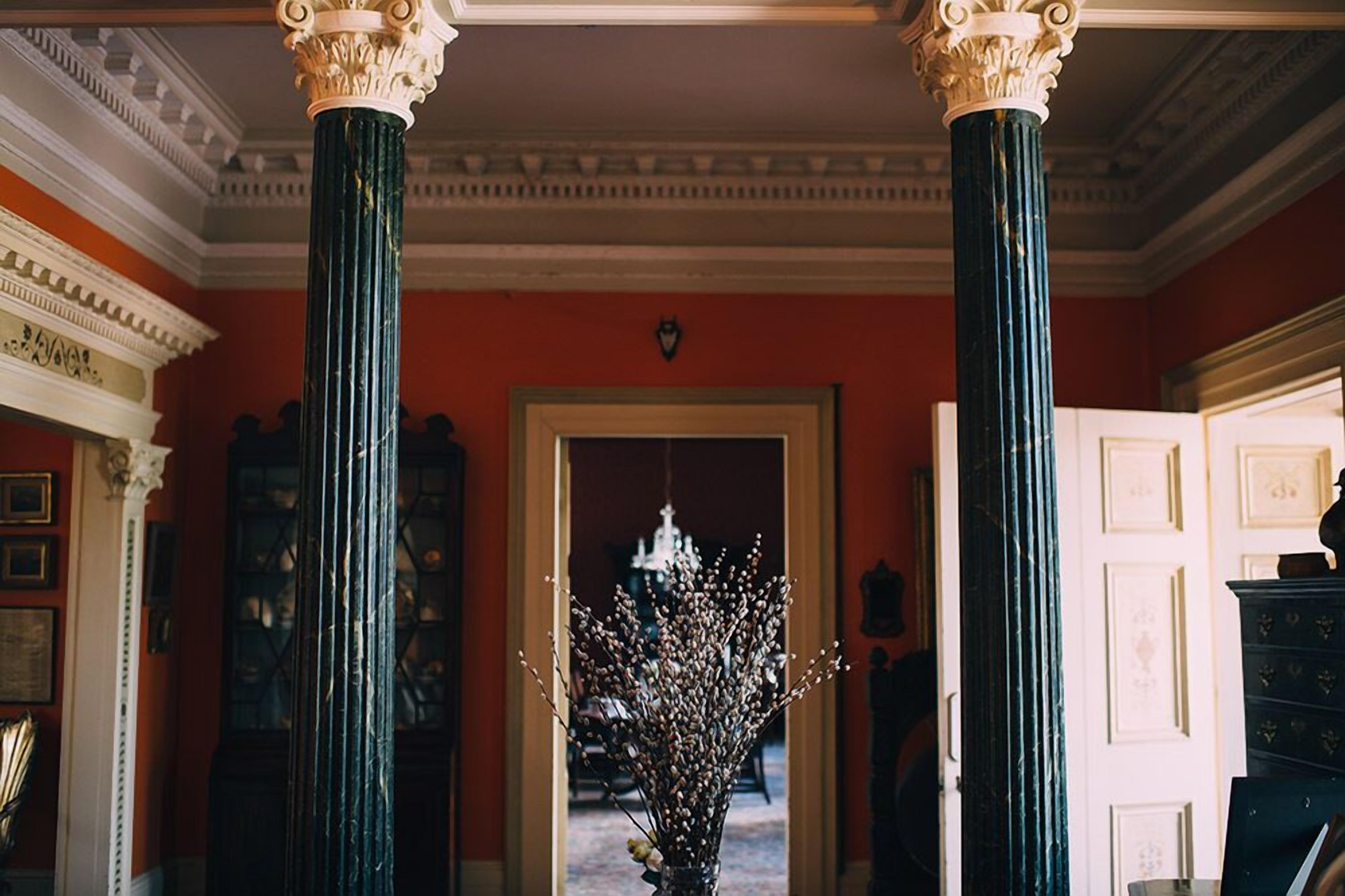 A hallway with two large columns, a chandelier, and a door leading to another room.