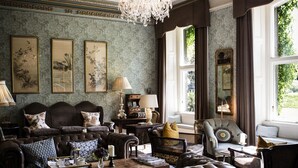 A traditional living room with a large, ornate chandelier, leather sofas, and a patterned rug. - Ballyvolane House (Kilcor)