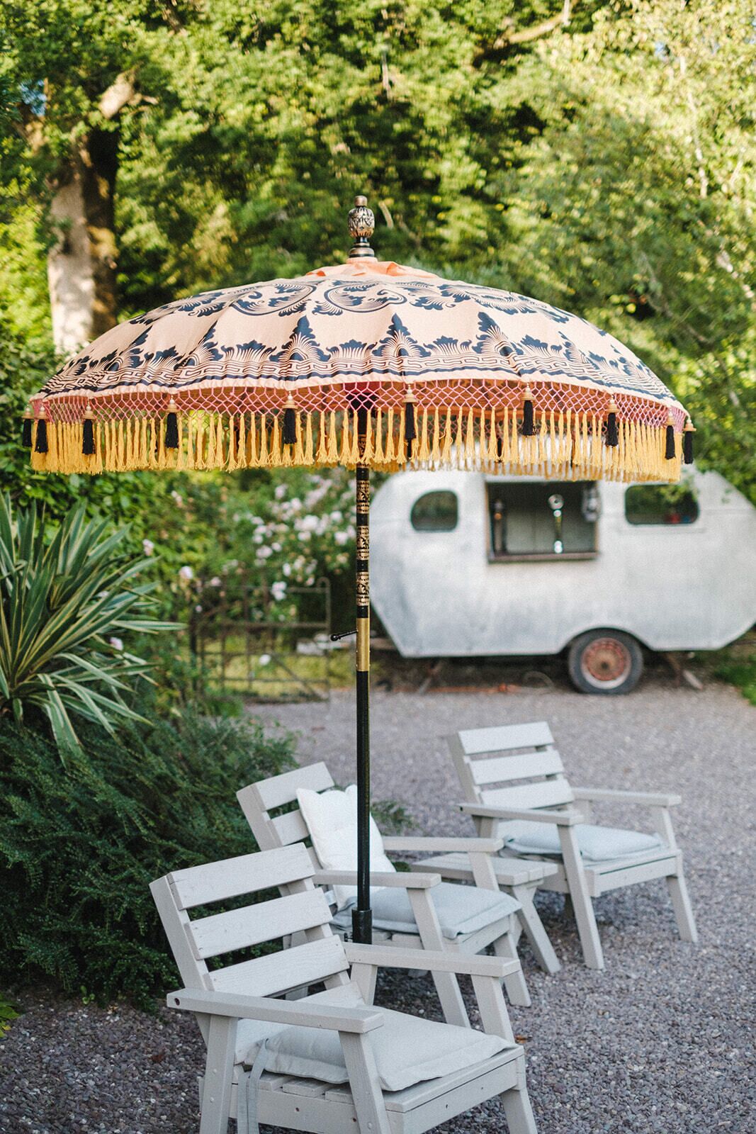A row of white outdoor chairs and a decorative umbrella with tassels.