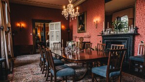 A formal dining room with a large wooden table, blue upholstered chairs, a chandelier, and a fireplace. - Ballyvolane House (Kilcor)