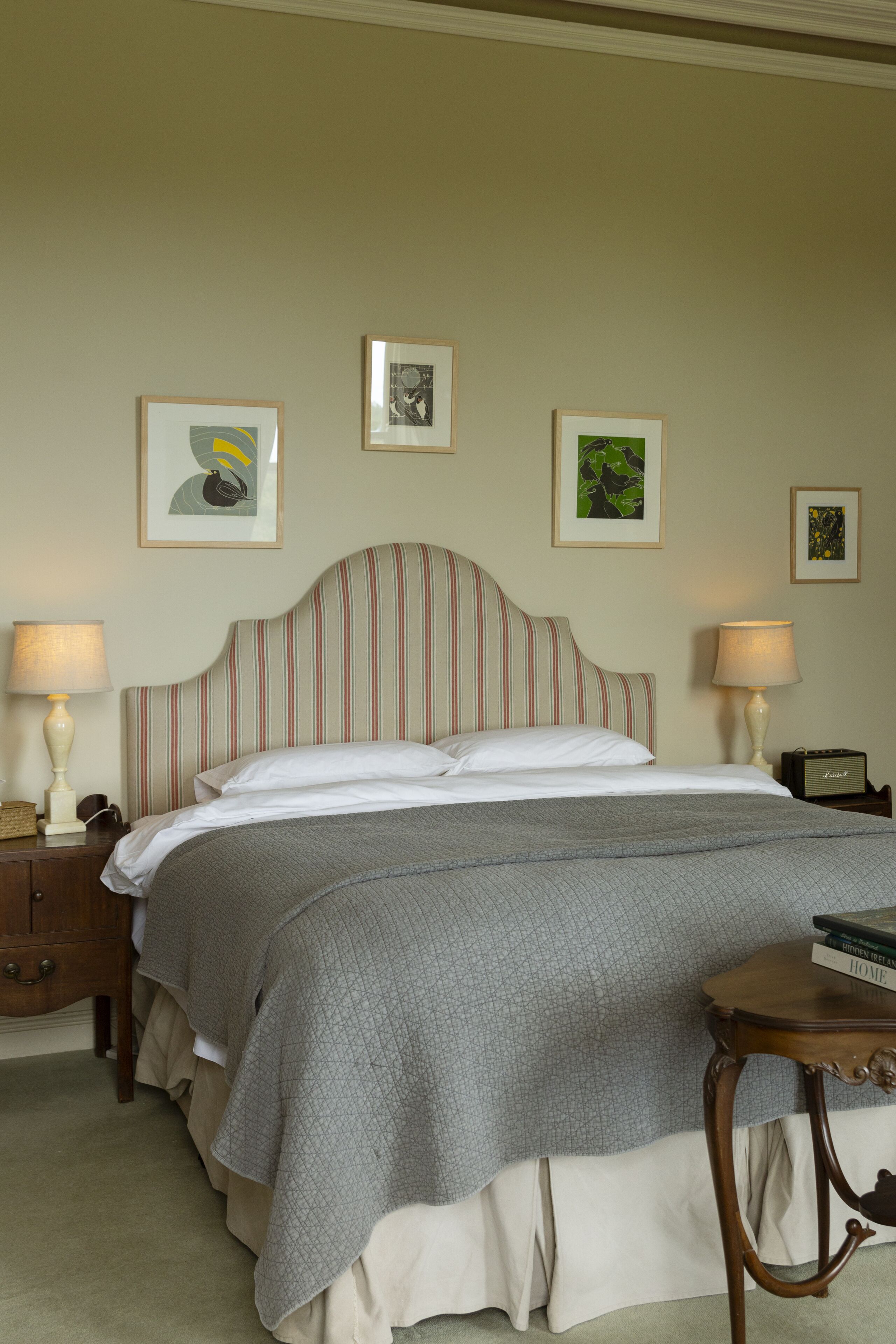 A neatly made bed with a striped headboard, two bedside lamps, and framed artwork on the wall.